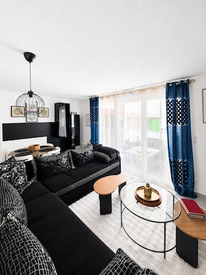 A modern living room with a black sofa, a glass coffee table, and a black TV stand. - New apartment, terrace & parking – Résidence Boréal, Montpellier (Monptellier)