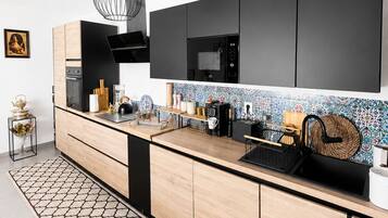 Une cuisine moderne avec un micro-ondes noir, des armoires en bois, un pare-feu décoré et un luminaire suspendu.