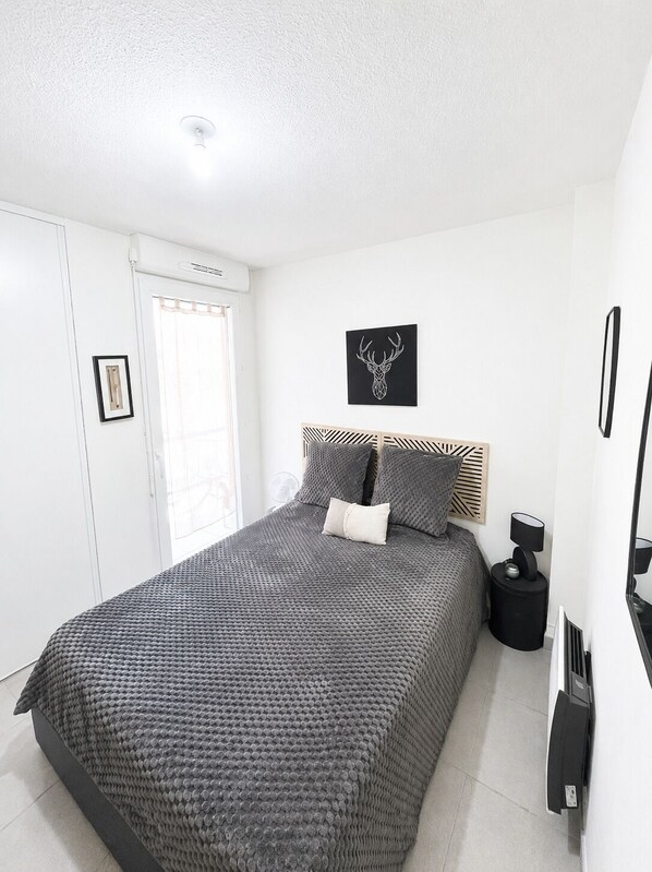 A modern bedroom with a large bed, a headboard with a geometric pattern, a wall-mounted picture of a deer head, and a bedside table with a lamp.