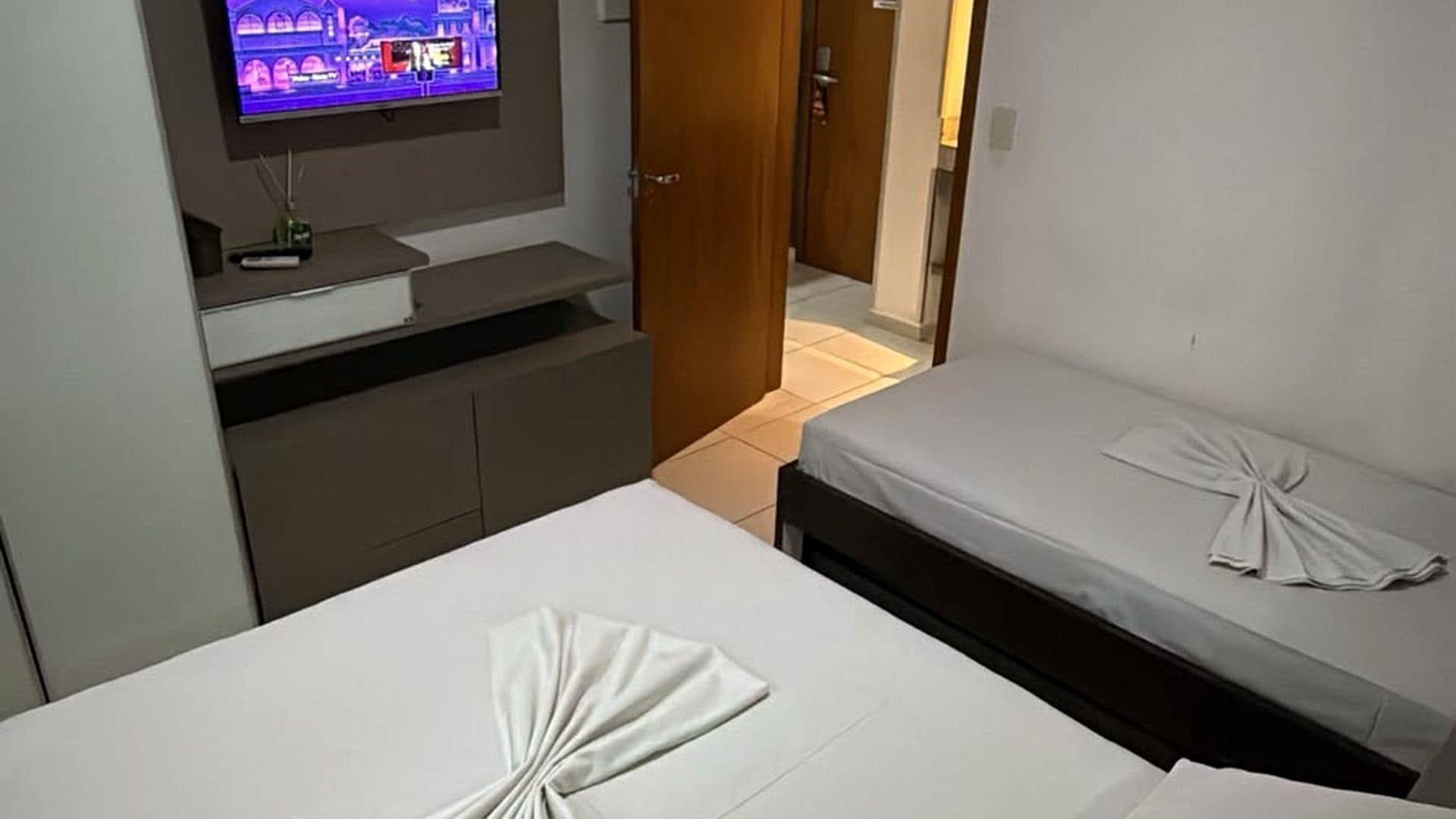 Quarto de hotel com uma cama, televisão na parede e porta para outro quarto.