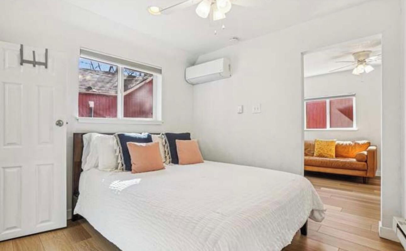Une chambre à coucher avec un lit, une fenêtre, un ventilateur de plafond et une vue sur une grange rouge, visible par la fenêtre.