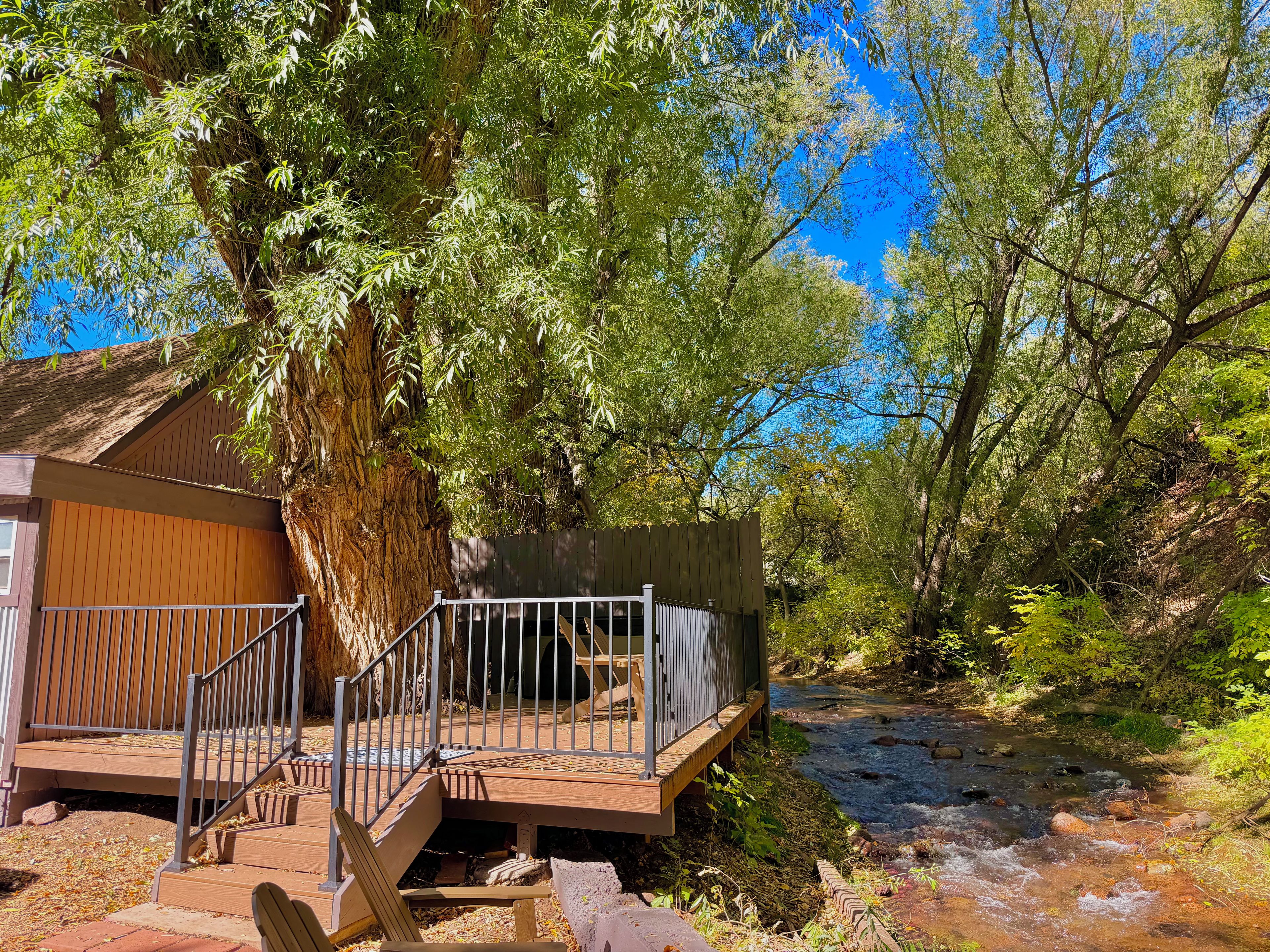Une cabane en bois dotée d’une terrasse et d’un escalier menant à un porche, entourée d’arbres et bordée par un ruisseau.
