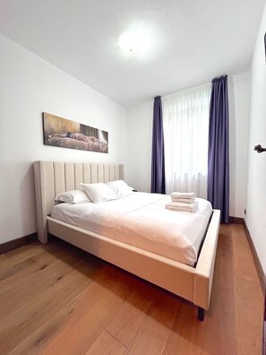 Ein Hotelzimmer mit einem Bett, einem Kopfteil, einem Bild an der Wand und einem Fenster mit Vorhängen.