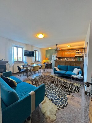 Ein Wohnzimmer mit einer Couch, einem Couchtisch und einem Fernseher. Es gibt eine Küchenzeile mit Schränken und einem Kühlschrank.