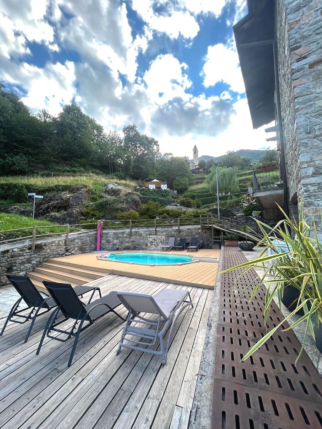 A wooden deck with a pool, lounge chairs, and a stone wall.