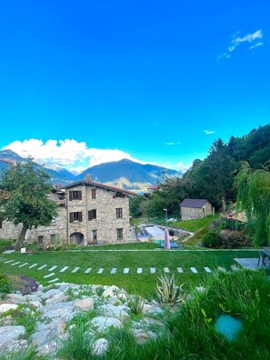 A stone building with a garden in front, surrounded by mountains and clear sky. - The Ancient Village (Vignola)