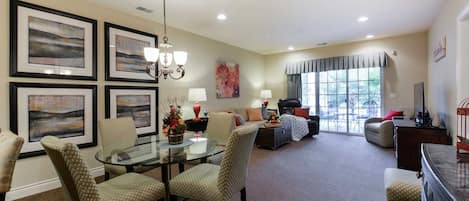 A spacious living room with a glass dining table, comfortable seating, and a large window offering a view of the outdoors.