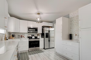 A modern kitchen with white cabinetry, stainless steel appliances, and a patterned backsplash. - Luxury, Romantic, Unique Retreat (Norcross)