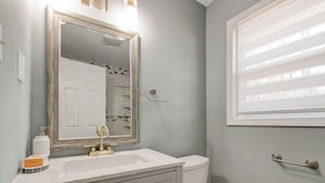 A bathroom with a white sink, a mirror, a toilet, and a window with blinds. - Luxury, Romantic, Unique Retreat (Norcross)