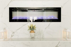 A modern bathroom with a marble countertop, a mounted fireplace, and two wall-mounted lanterns.
