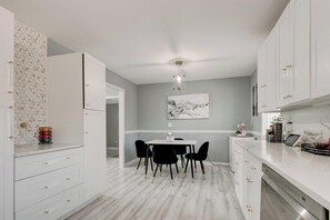 A modern kitchen with white cabinetry, a dining area with black chairs, and a grey accent wall.