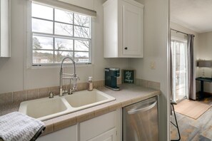 A kitchen with a double sink, a coffee maker, and a view of the outside.