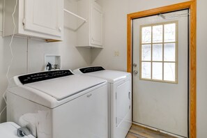 A laundry room with two white washers and dryers, a wooden door, and a window.