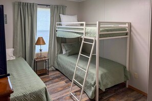A bunk bed room with a ladder, a bedside table with a lamp, and a window with curtains.