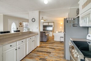 A compact kitchen with a built-in stove, a dining area with a grey sofa, and a TV in the background.