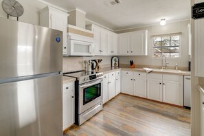 A kitchen with white cabinets, stainless steel appliances, a microwave, and a window with a view.