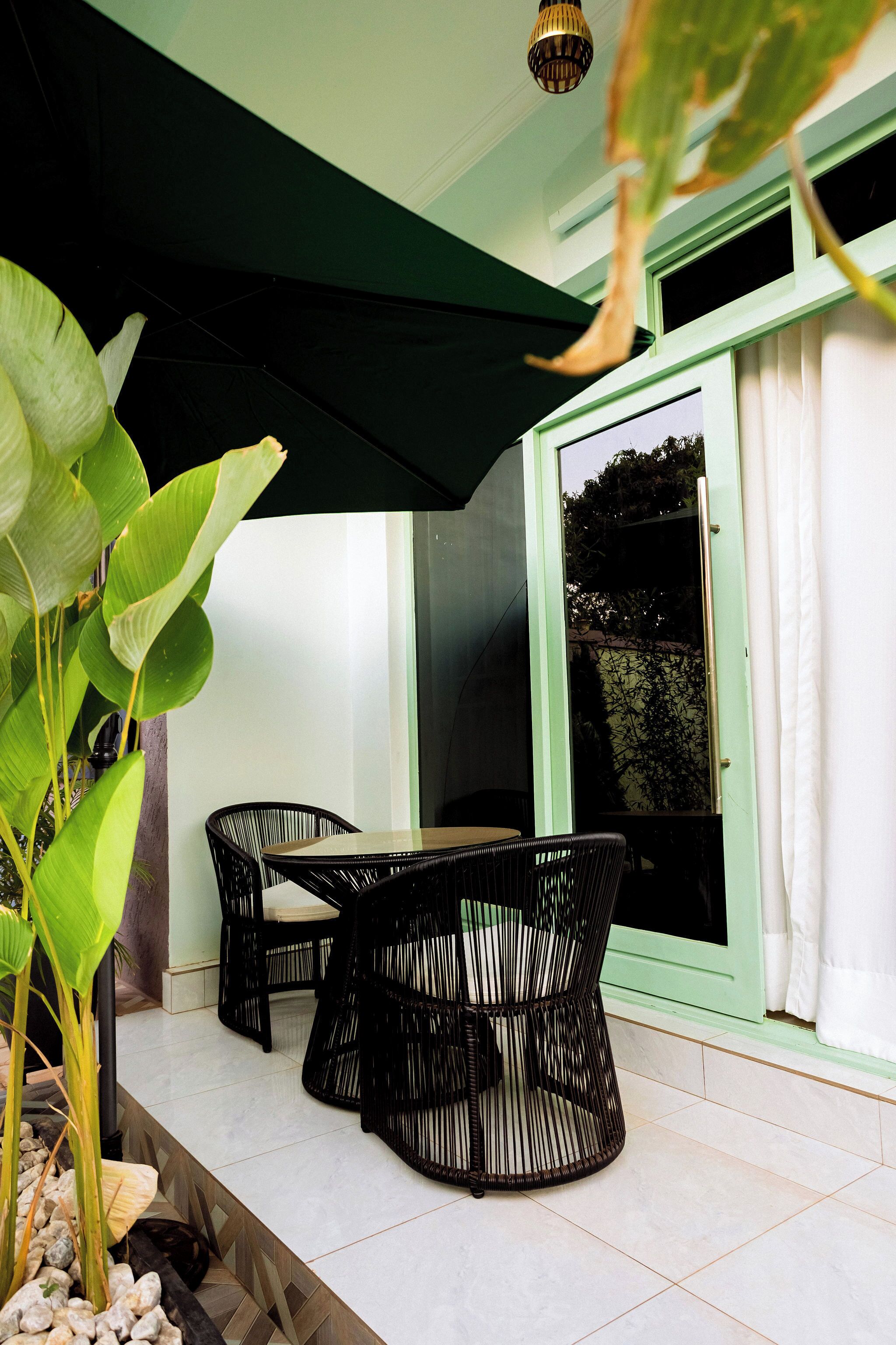 An outdoor seating area with two black wicker chairs and a table, a green awning, and a potted plant.
