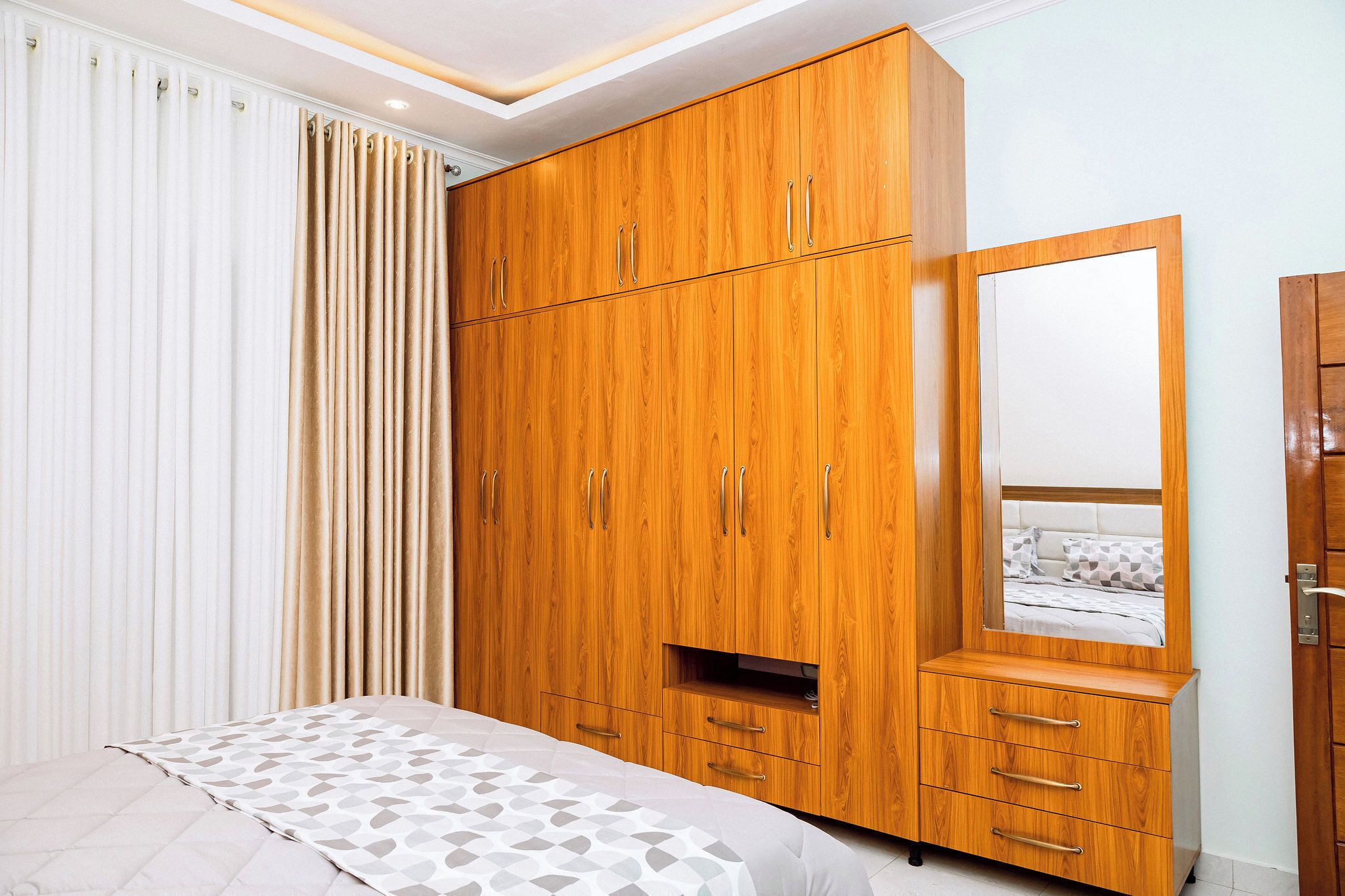 Une chambre avec une armoire en bois, un lit avec une literie à motifs et un grand miroir.
