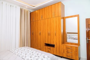 Une chambre avec une armoire en bois, un lit avec une literie à motifs et un grand miroir.