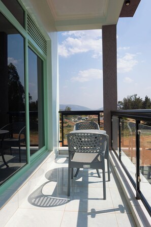 Een balkon met een tafel en stoelen, een glazen deur en uitzicht op het landschap.