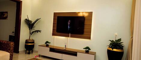 Un salon moderne avec un téléviseur à écran plat fixé à un mur en bois, un canapé, une table basse agrémentée d’une plante, et deux plantes en pot posées sur des tables d’appoint.