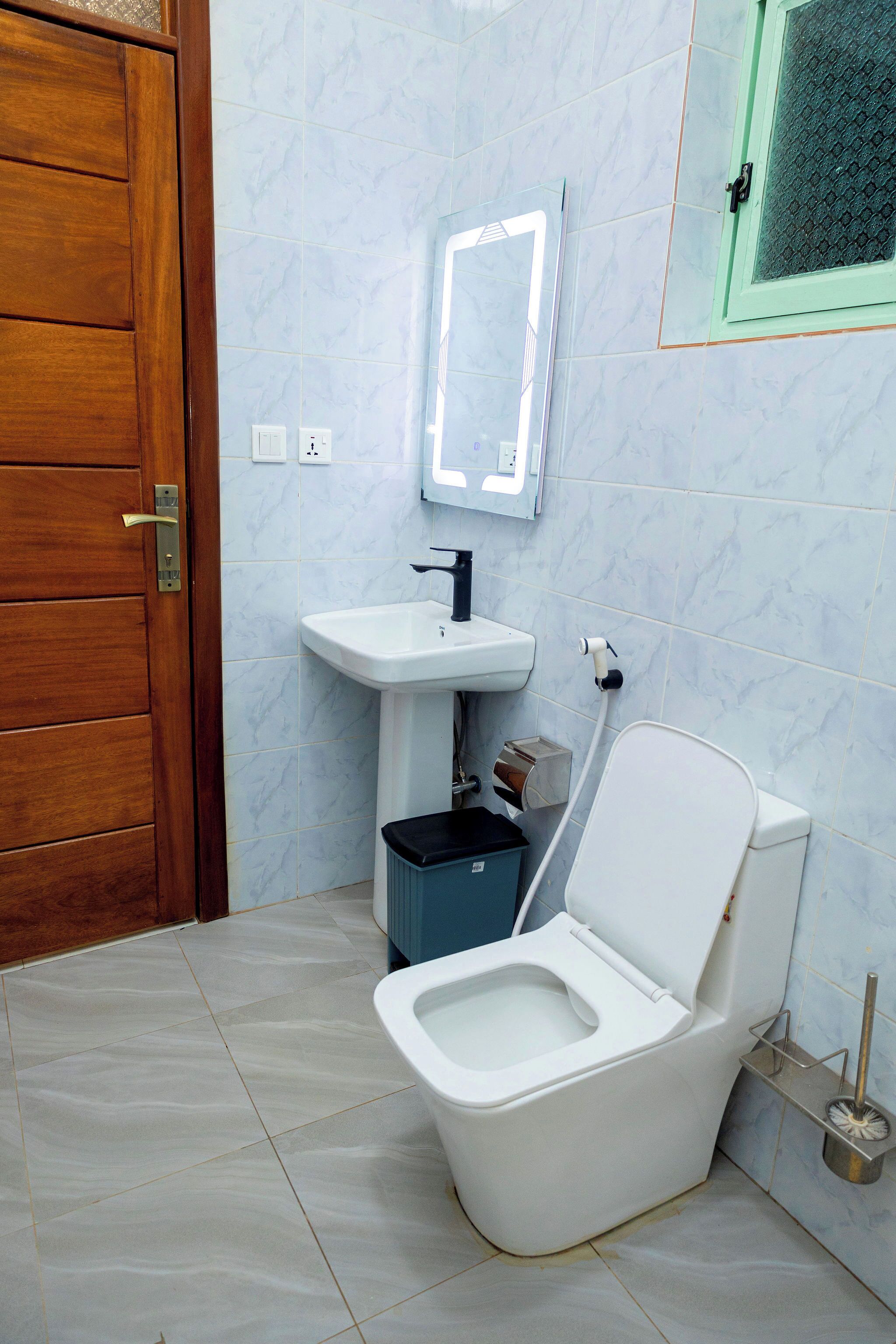 A bathroom with a wooden door, a white sink, a toilet, and a mirror.