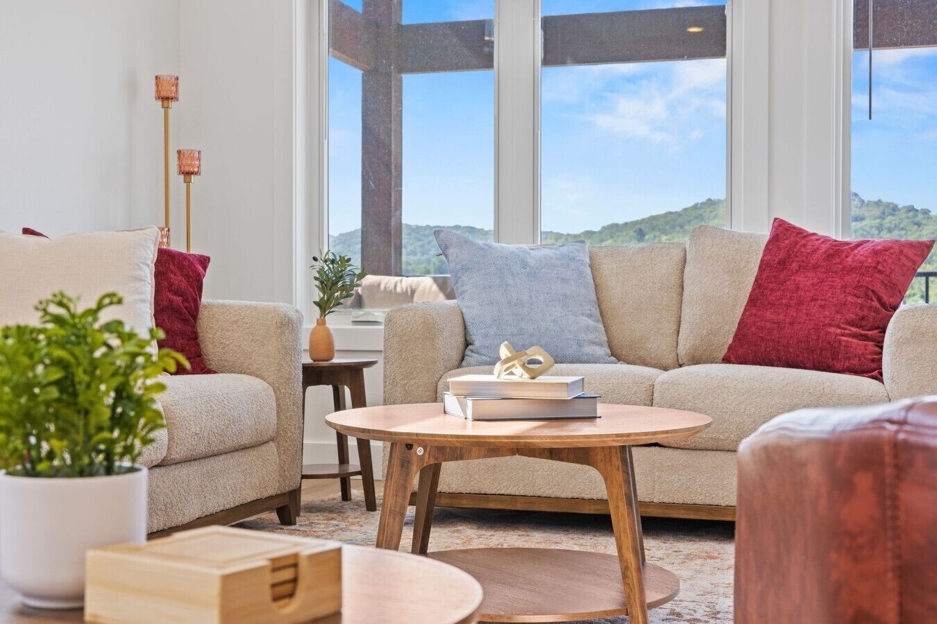 A modern living room with a sofa, a coffee table, and a view of a green landscape through large windows.