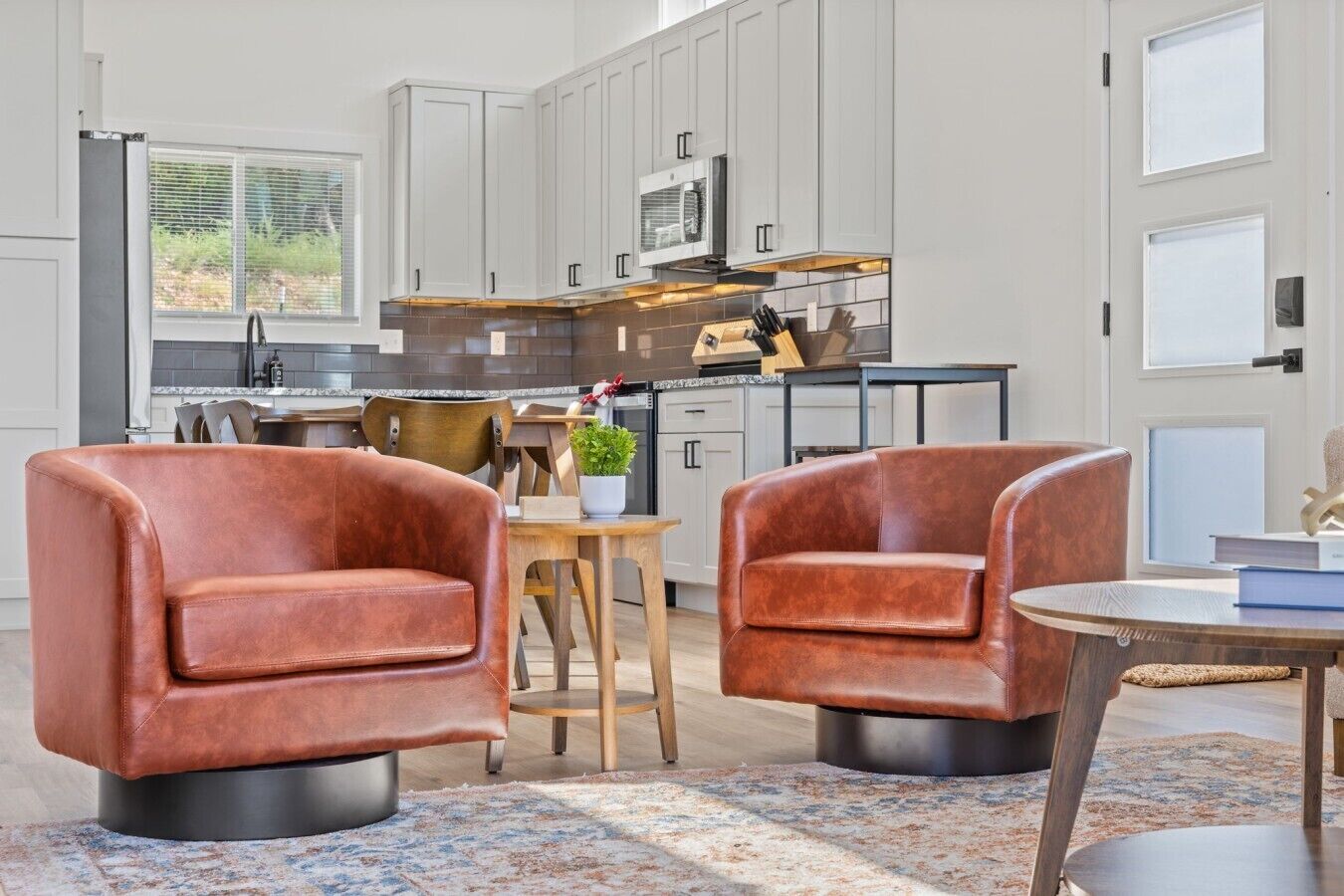 A modern kitchen with white cabinets, a microwave, and a dining area with two leather armchairs and a small table.