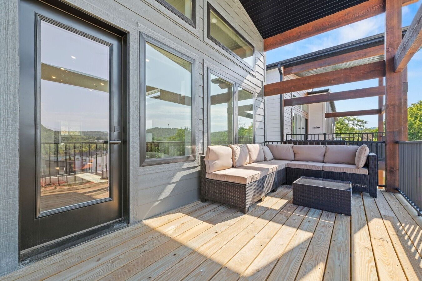 A covered outdoor deck with a sectional sofa and a small table, large windows, and a wooden deck floor.