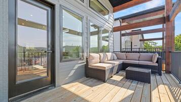 A covered outdoor deck with a sectional sofa and a small table, large windows, and a wooden deck floor.