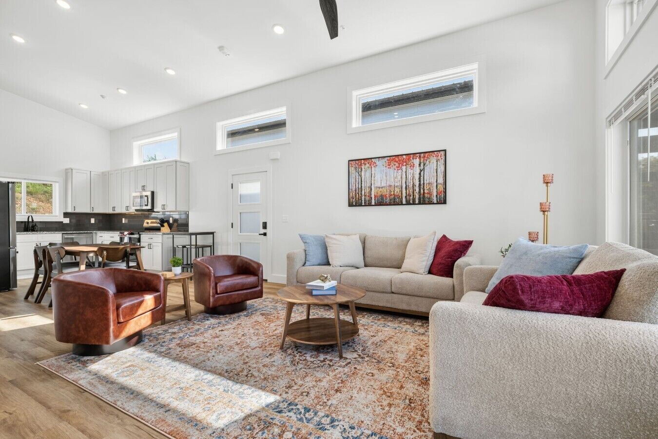 A spacious living area with a sofa, armchair, and coffee table, a kitchen in the background, and a painting on the wall.