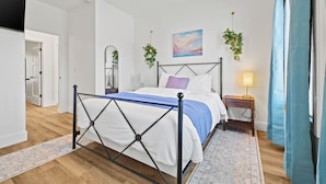 A bedroom with a metal bed frame, a bedside table with a lamp, a painting on the wall, and a hanging plant. - Luxury Getaway | Lake View + Fire Table (Reeds Spring)