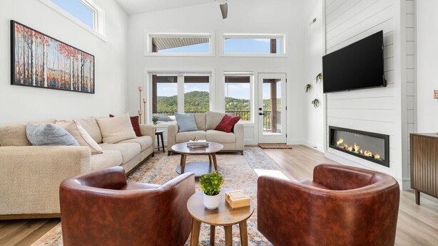 A spacious living room with a fireplace, a ceiling fan, and a large painting. - Luxury Getaway | Lake View + Fire Table (Reeds Spring)