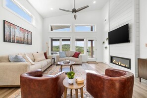 A spacious living room with a fireplace, a ceiling fan, and a large painting.