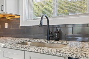 A kitchen with a granite countertop, a stainless steel sink, and a window with blinds.