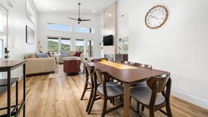A spacious living area with a wooden dining table, comfortable seating, and a large window offering a view of the outdoors. - Luxury Getaway | Lake View + Fire Table (Reeds Spring)