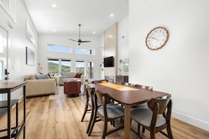 A spacious living area with a wooden dining table, comfortable seating, and a large window offering a view of the outdoors. - Luxury Getaway | Lake View + Fire Table (Reeds Spring)