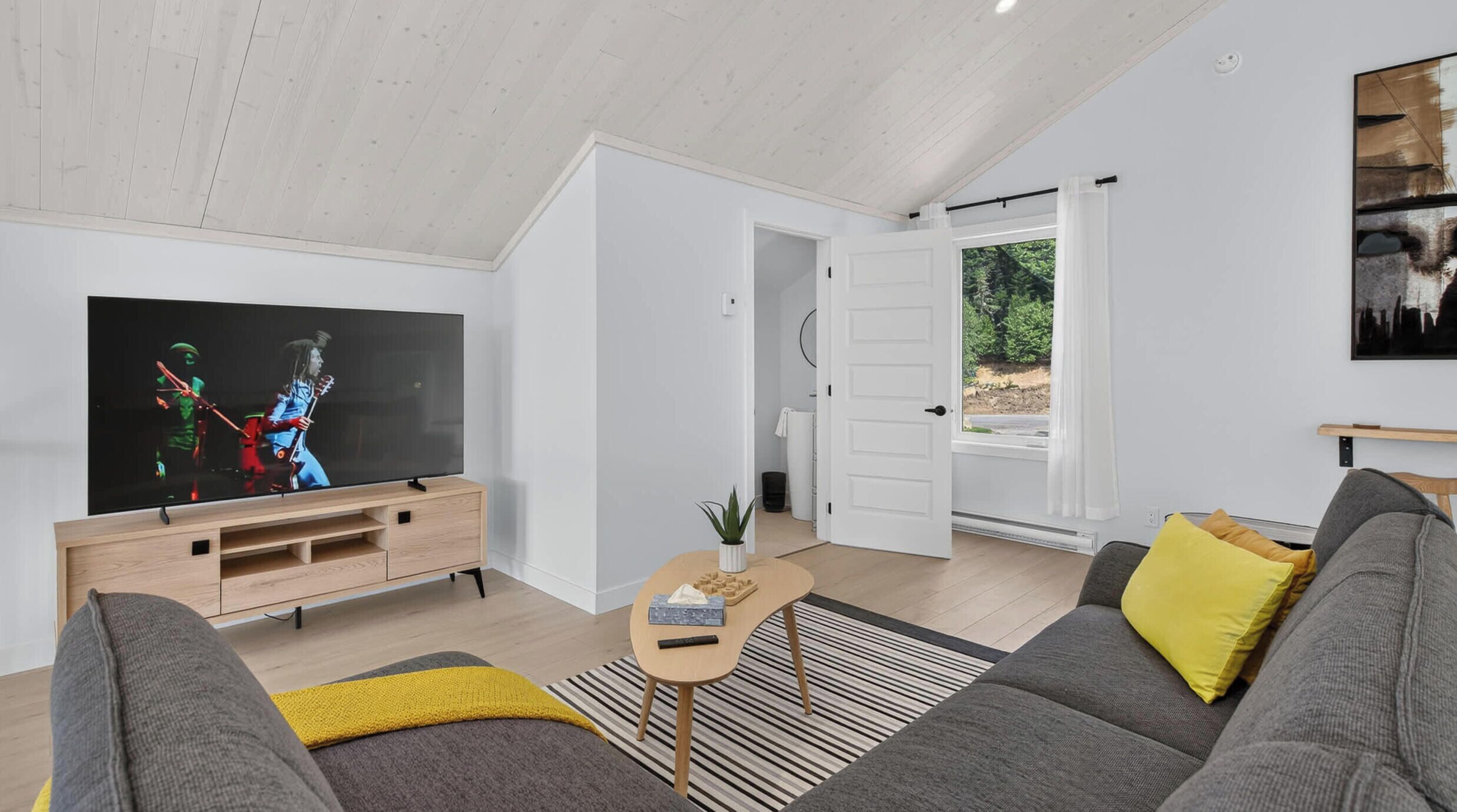 A modern living room with a flat-screen TV, grey sofa, and a wooden coffee table.