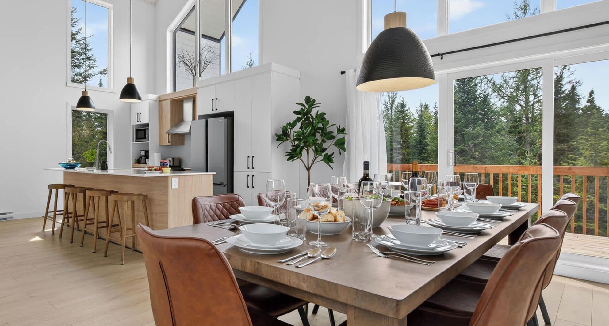 A modern dining area with a wooden table set for a meal, large windows, and a view of the outdoors.