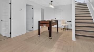 Une pièce avec un baby-foot, un bureau avec un ordinateur et une chaise. Un escalier mène à un autre niveau.