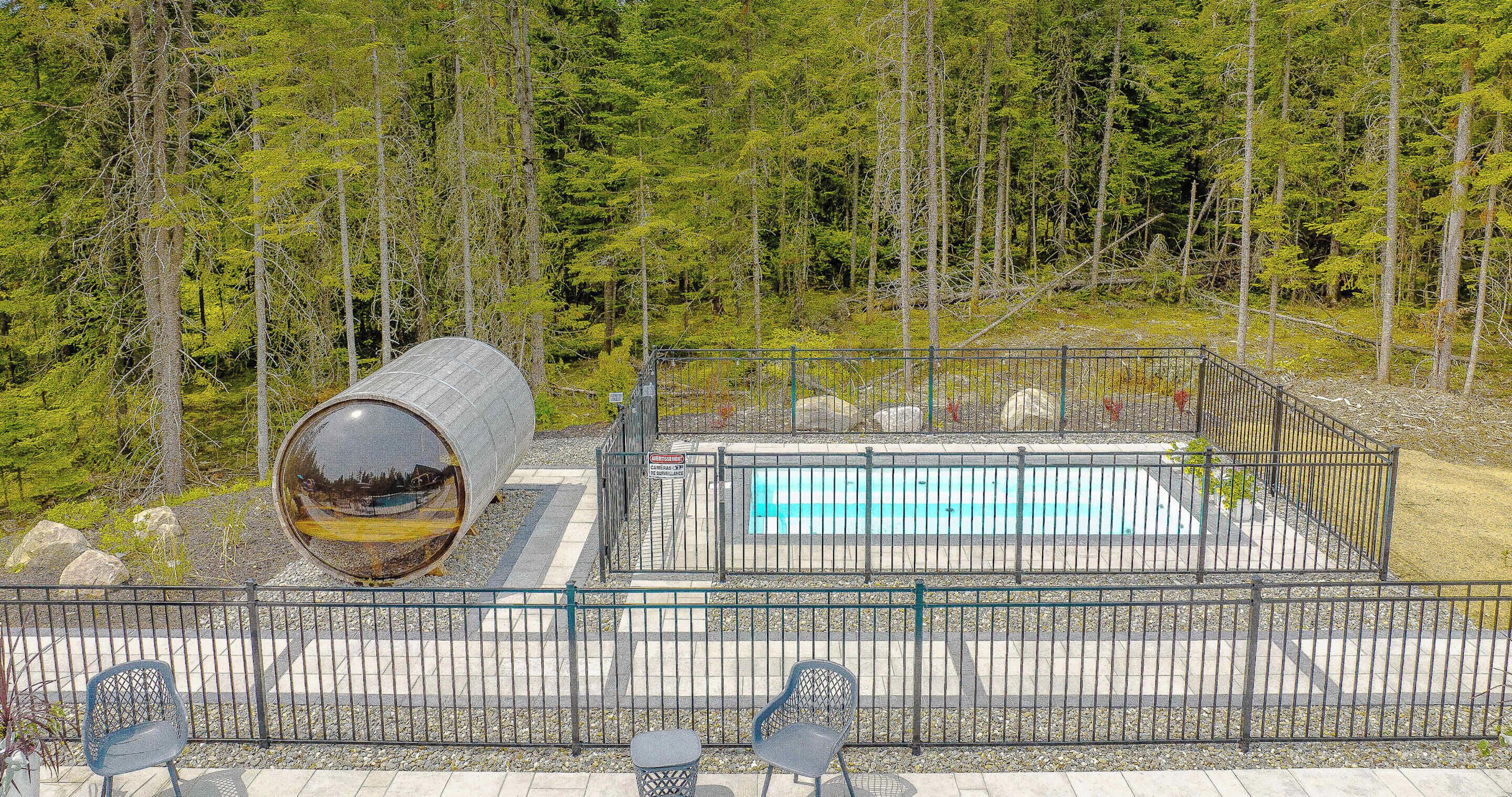 A swimming pool with a metal fence, surrounded by a forested area.