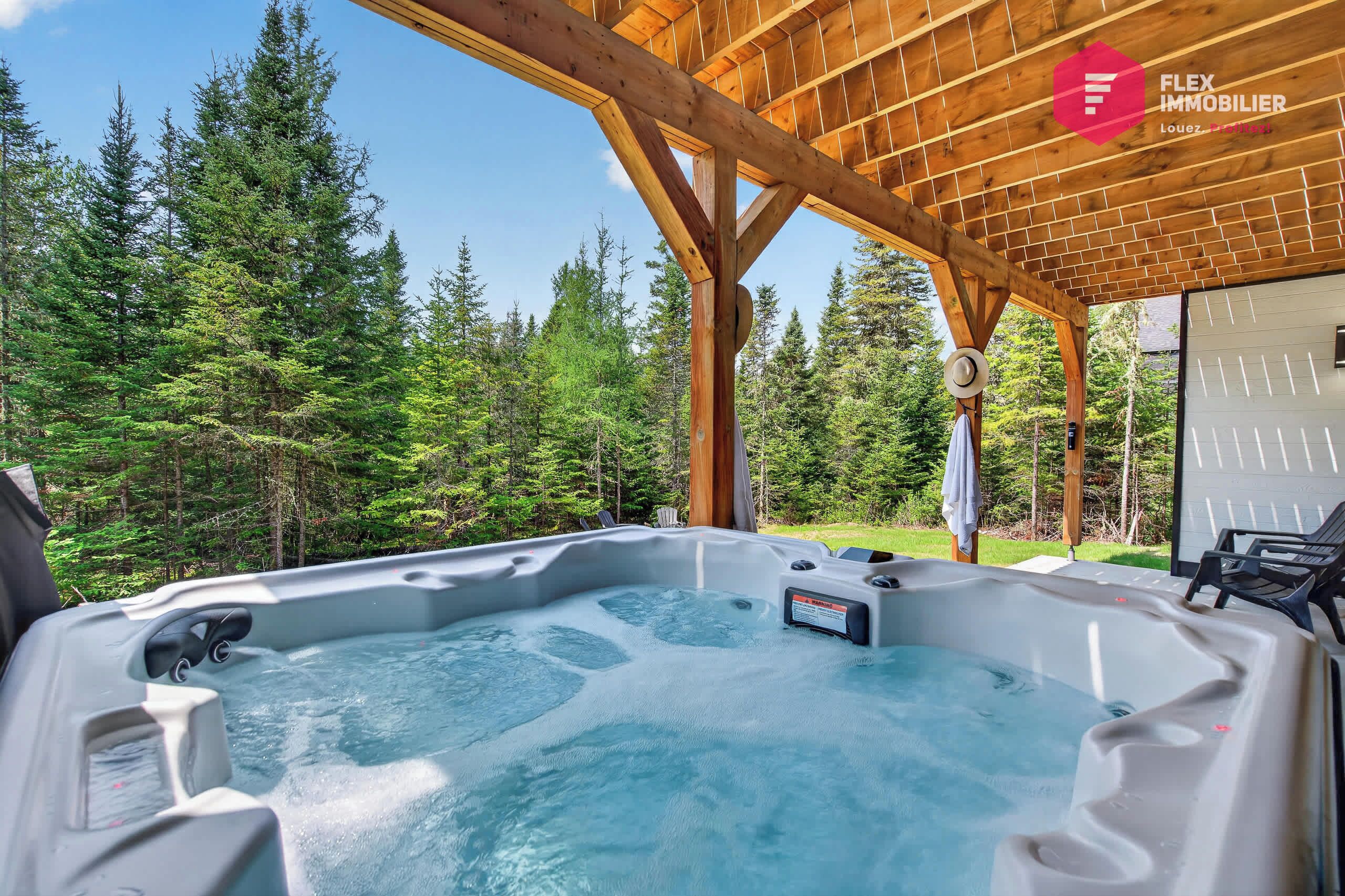 A hot tub under a wooden pergola with a forest backdrop.
