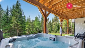 A hot tub under a wooden pergola with a forest backdrop.