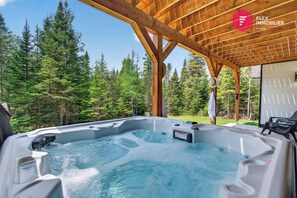 A hot tub under a wooden pergola with a forest backdrop.