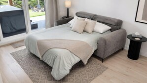 A bedroom with a bed, pillows, a bedside table, a lamp, a small table with a tissue box, and a view of the outdoors through a sliding door. - Jadeheim - Chalet 12 pers Spa et Sauna prives - Resort pres de Quebec (Shannon)