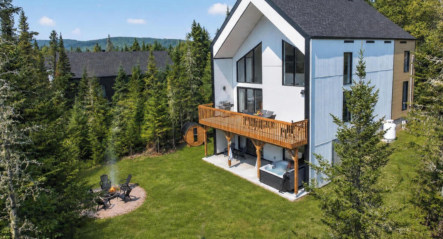 A modern two-story house with a wooden deck, a hot tub, and a fire pit in the backyard.