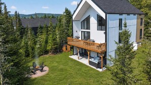 A modern two-story house with a wooden deck, a hot tub, and a fire pit in the backyard.