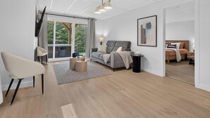 A modern living room with a sofa, a chair, a coffee table, and a large window with a view of greenery.