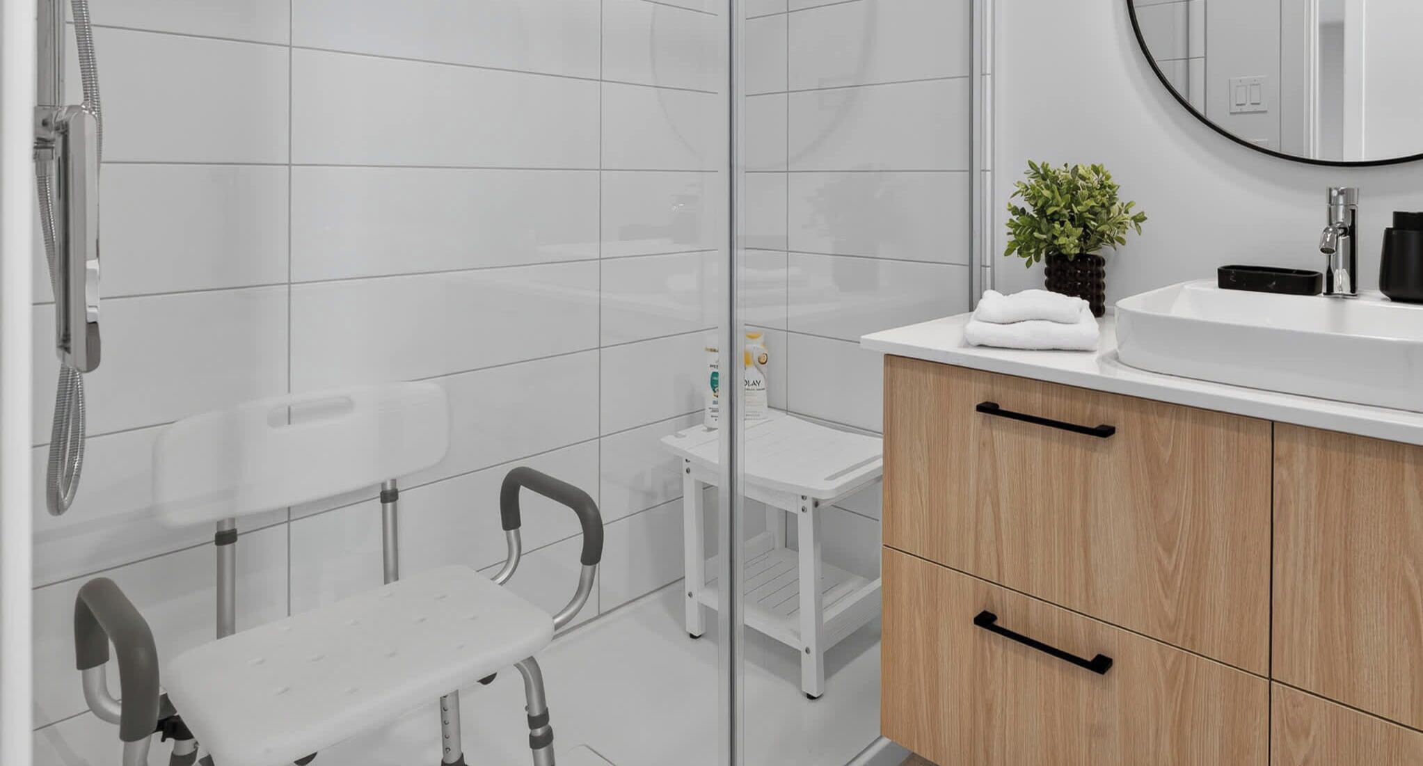 Une salle de bain moderne avec des carreaux blancs, une douche, un lavabo avec un miroir et une petite table.
