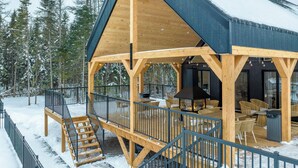 A wooden cabin with a covered deck, outdoor seating, and a staircase leading to the deck.